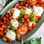 Green serving dish with tomatoes, burrata and basil. Lots of dressing and seasoning, up close