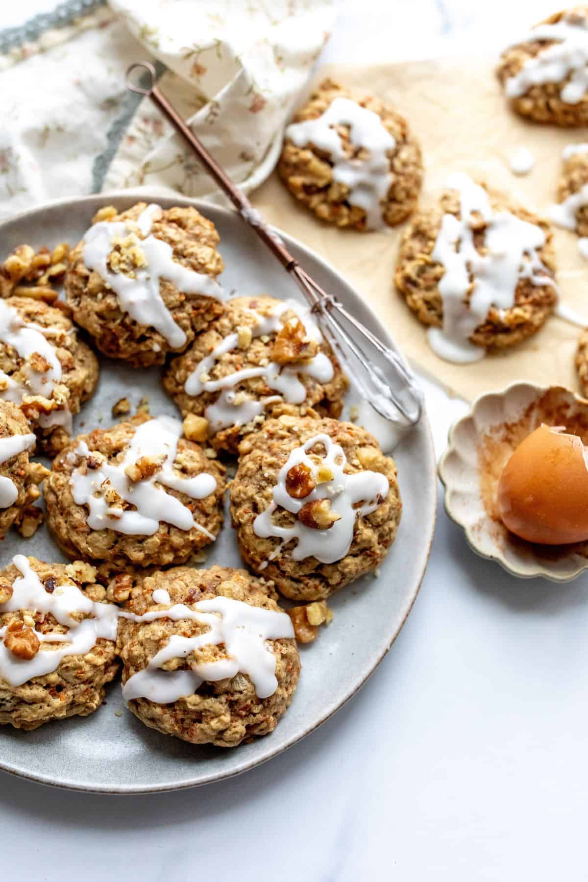 carrot cake cookies on a white plate with a whisk to the side.