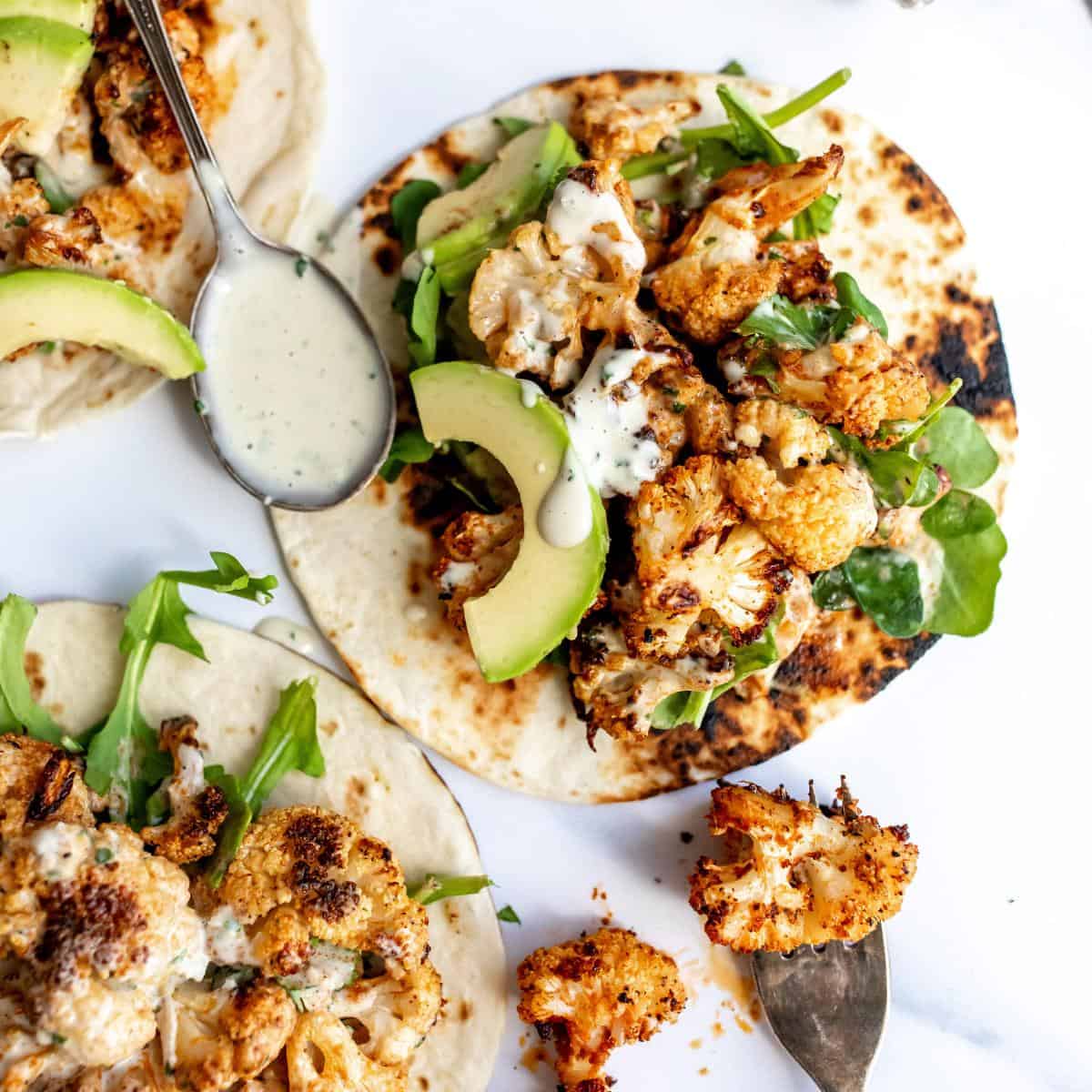 Roasted cauliflower tacos with a smoky sauce on a white counter with a spoon on the side.