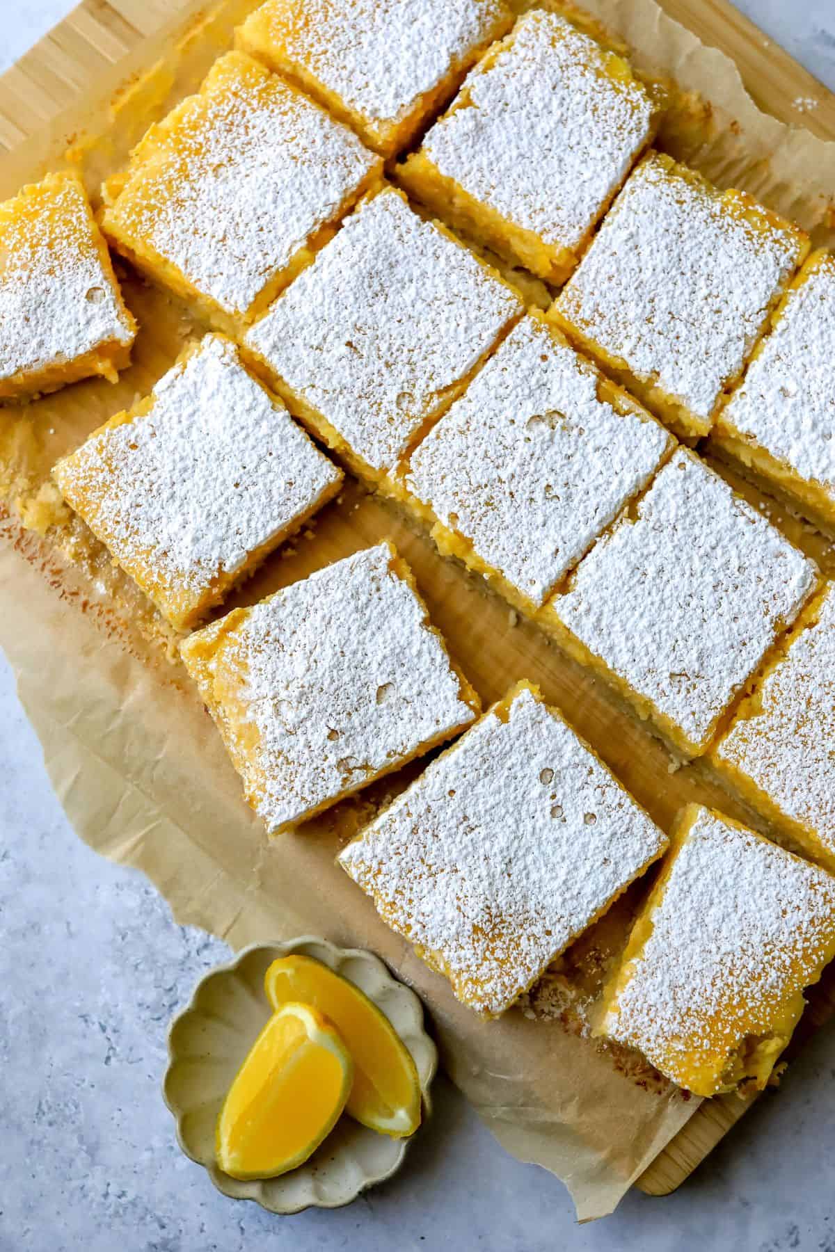 Lemon Cookie Bars on a wooden cutting board with lemons.