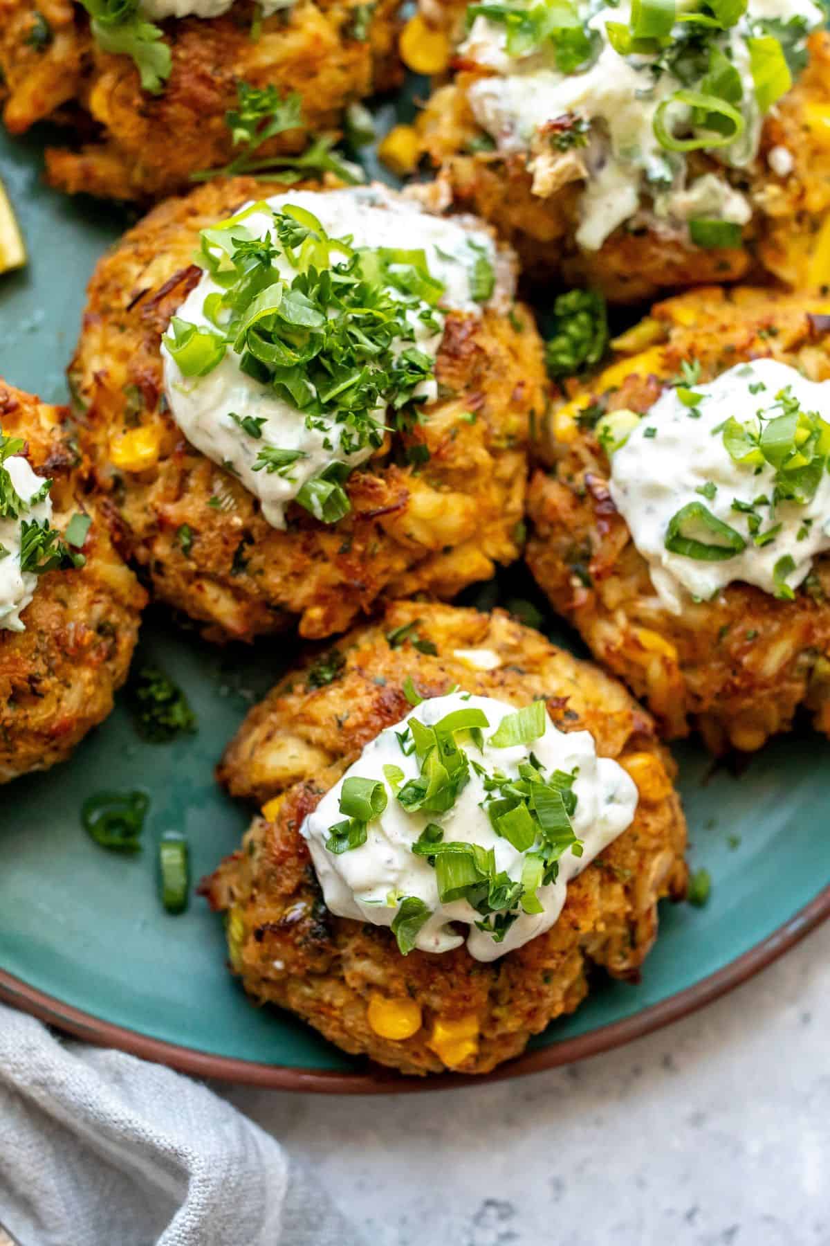 Up close photo of Maryland Crab Cakes on a green ceramic plate with two forks on the side and lemons. 