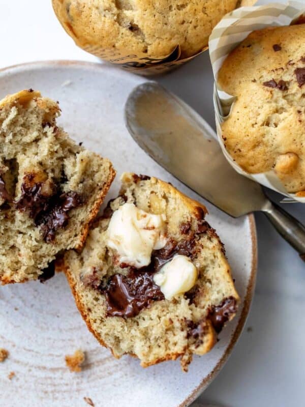 Chocolate Chunk Banana Muffins on a white ceramic plate with a butter knife to the side.