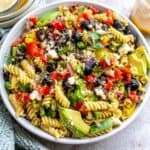 White ceramic bowl with zesty pasta salad in it with Italian dressing on the side. Up close photo.