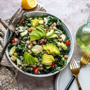 White bowl with kale and chickpeas, loads of veggies and dressing on the top.
