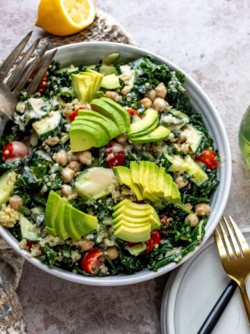 White bowl with kale and chickpeas, loads of veggies and dressing on the top.