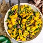 Mango and Avocado Salsa in a white bowl with a spoon in it and a green glass.