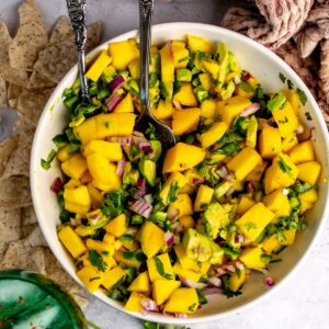 Mango and Avocado Salsa in a white bowl with a spoon in it and a green glass.