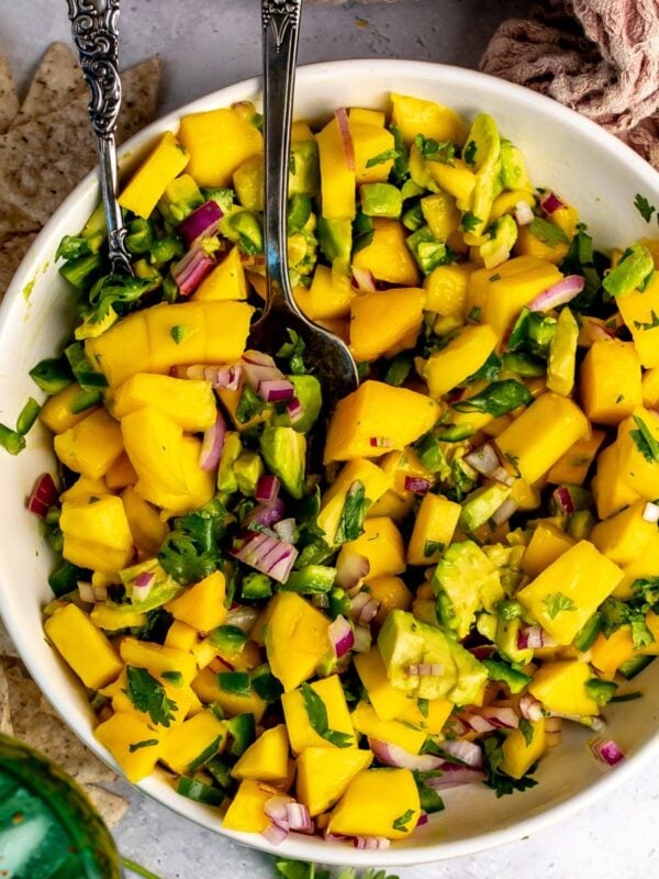 Mango and Avocado Salsa in a white bowl with a spoon in it and a green glass.