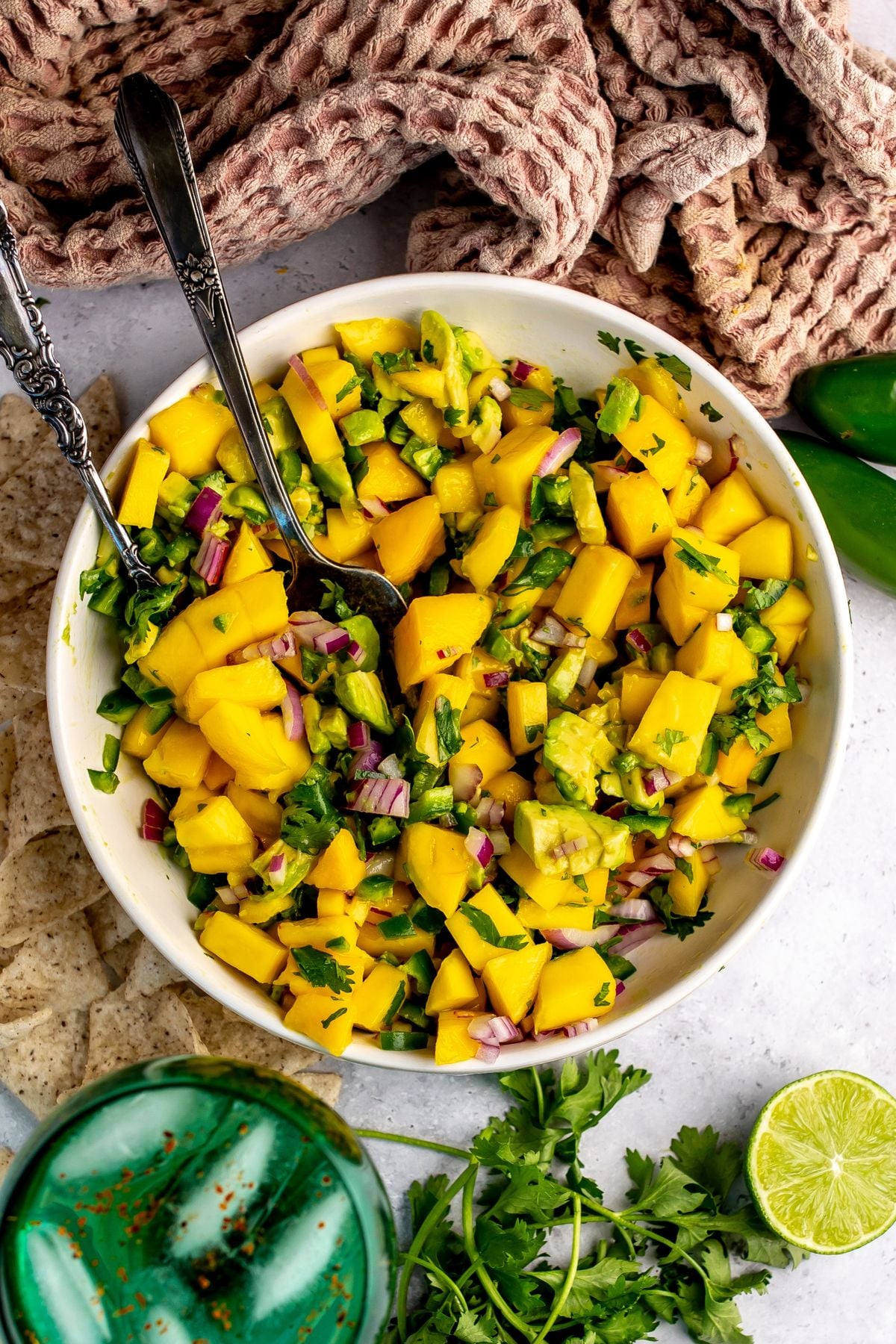Mango and Avocado Salsa in a white bowl with a spoon in it and a green glass.