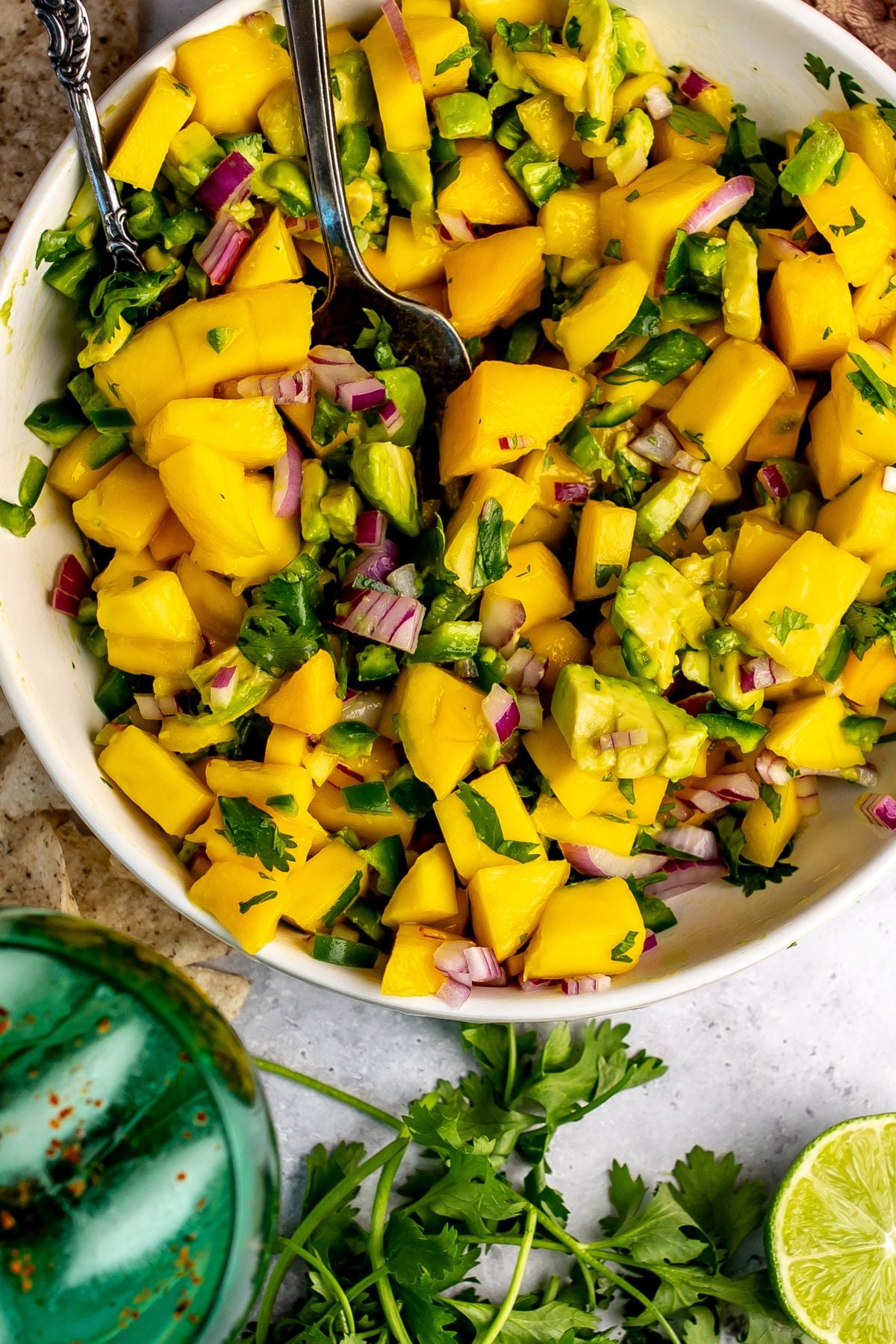 Mango and Avocado Salsa in a white bowl with a spoon in it and a green glass.