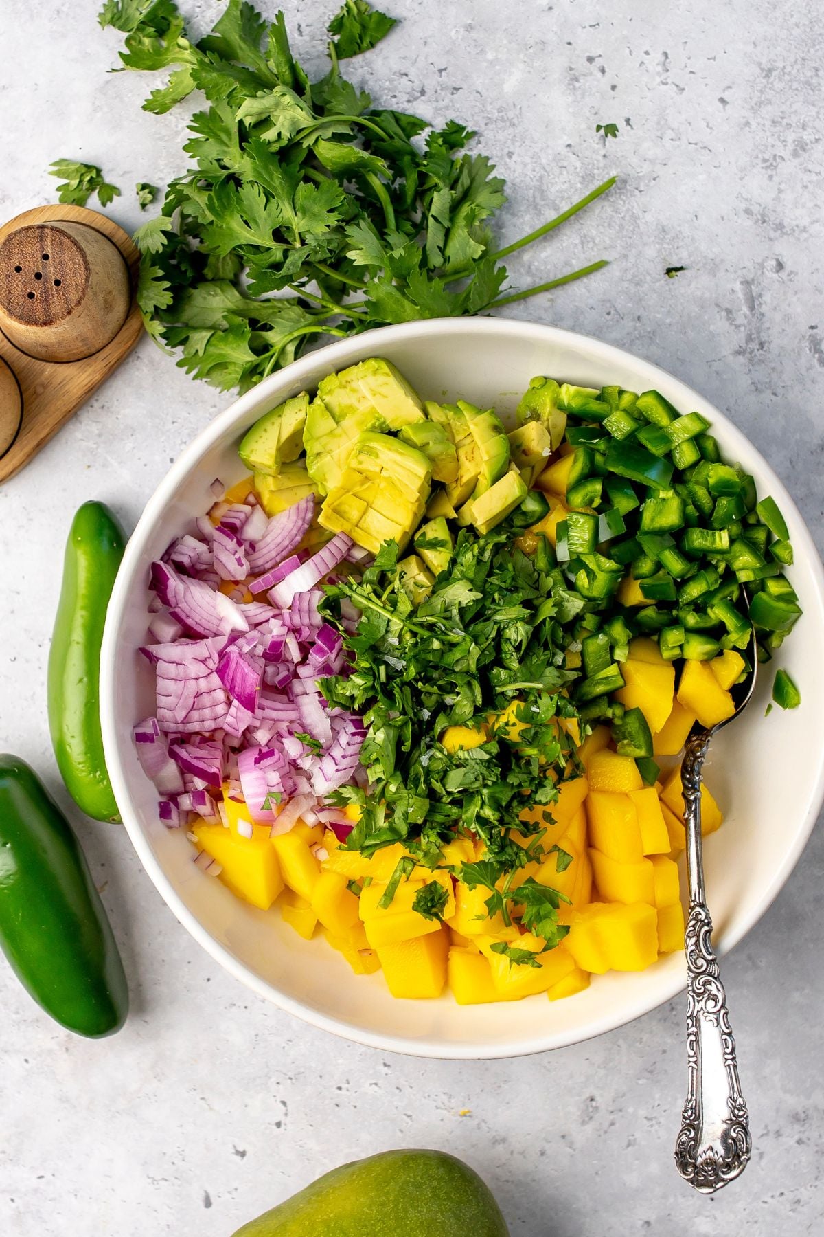 Avocado, jalapeño and mango all piled up in a white bowl with cilantro.