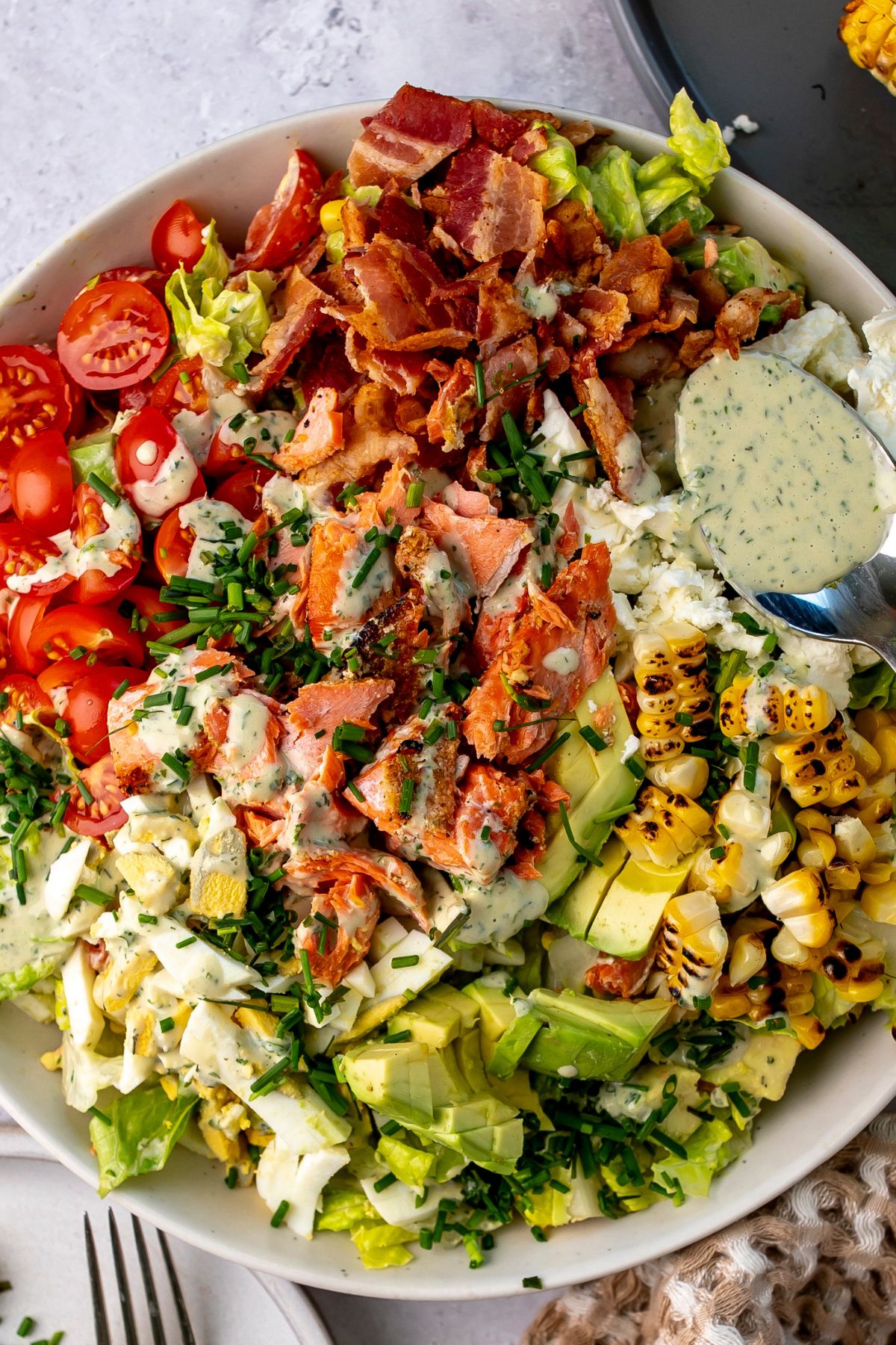 Salmon cobb salad in a bowl with a spoonful of dressing.