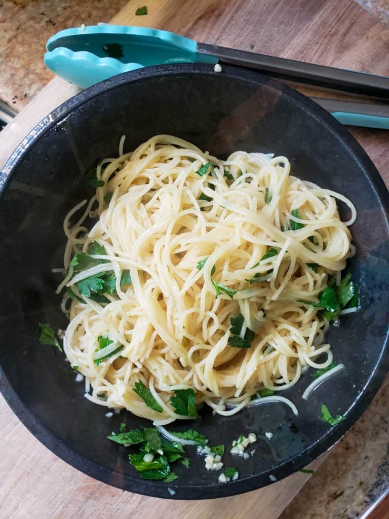Cooked pasta in a bowl tossed with the olive oil and herb dressing.