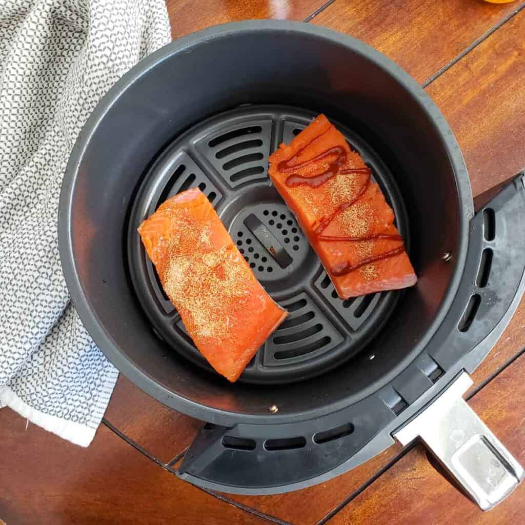 Salmon placed in an air fryer, skin side down with seasonings on top. 