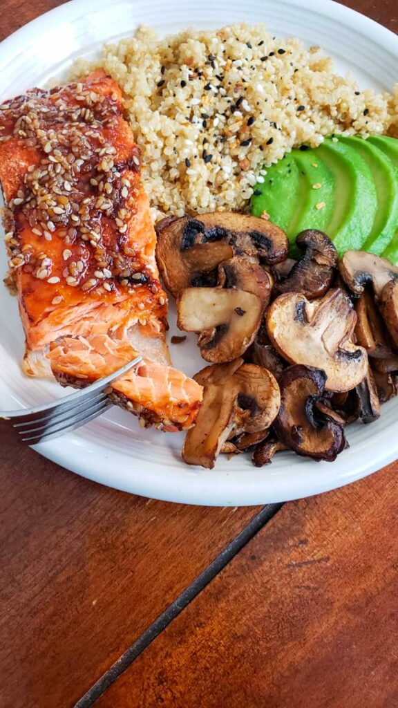 Up close Salmon on a white plate with quinoa, avocado, mushrooms and seasoning.