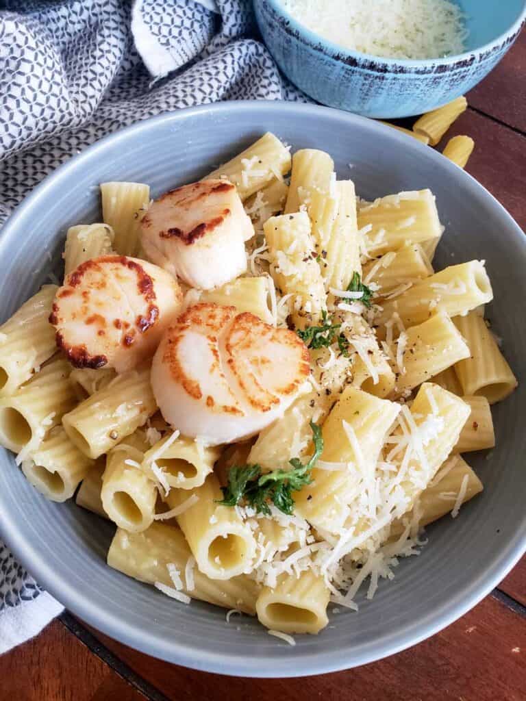 Healthier Cacio e PePe in a gray bowl with fresh parsley on top for color. seared scallops are on top to show you can top with a protein.