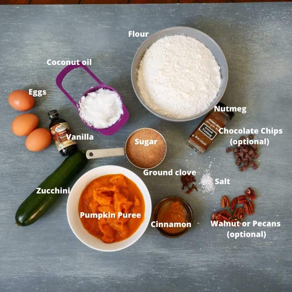 All the ingredients needed to make this pumpkin zucchini bread layer out on a grey board and labeled.