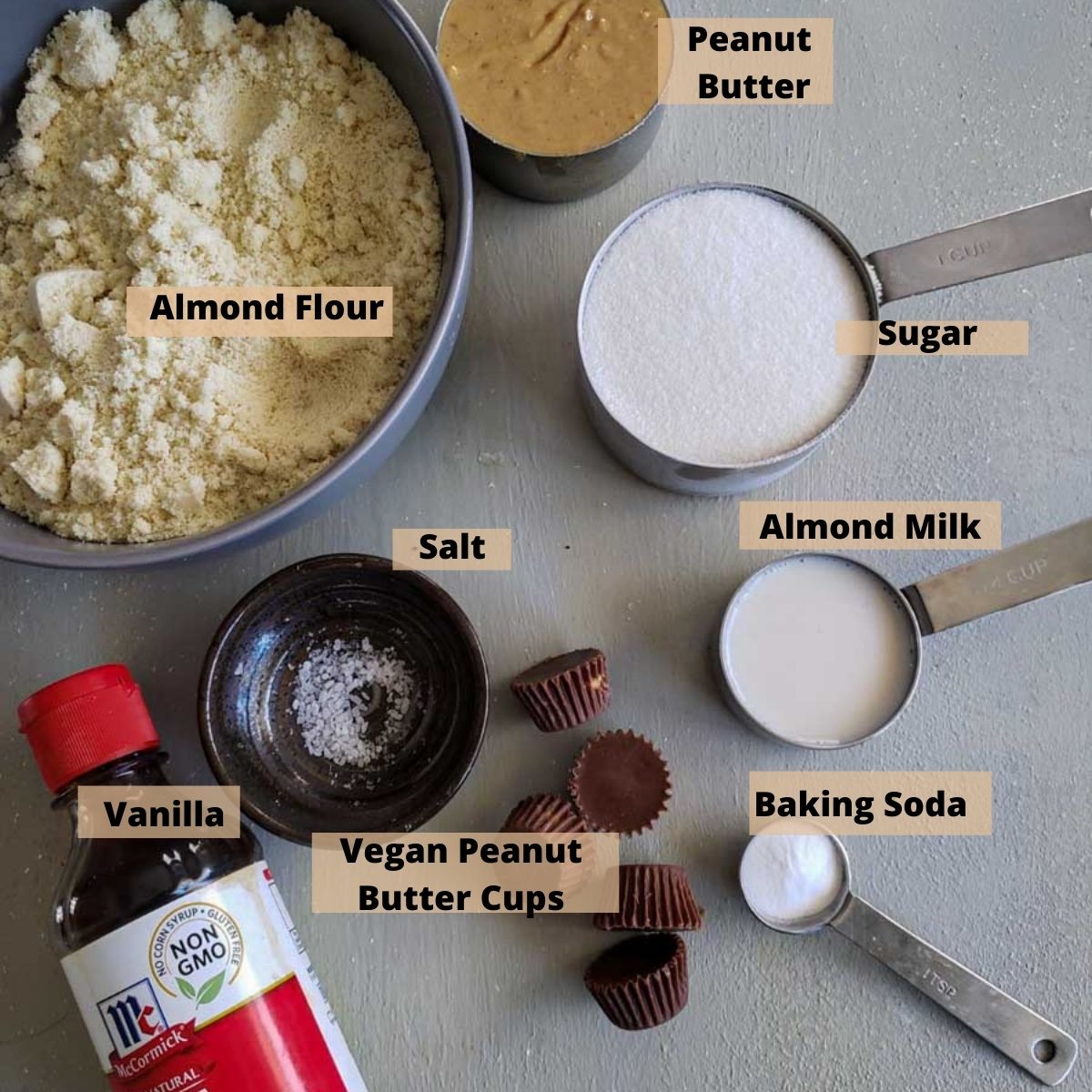 All the ingredients for this recipe on a grey board. Almond Flour, peanut butter, almond milk, sugar, salt, vanilla and baking soda.