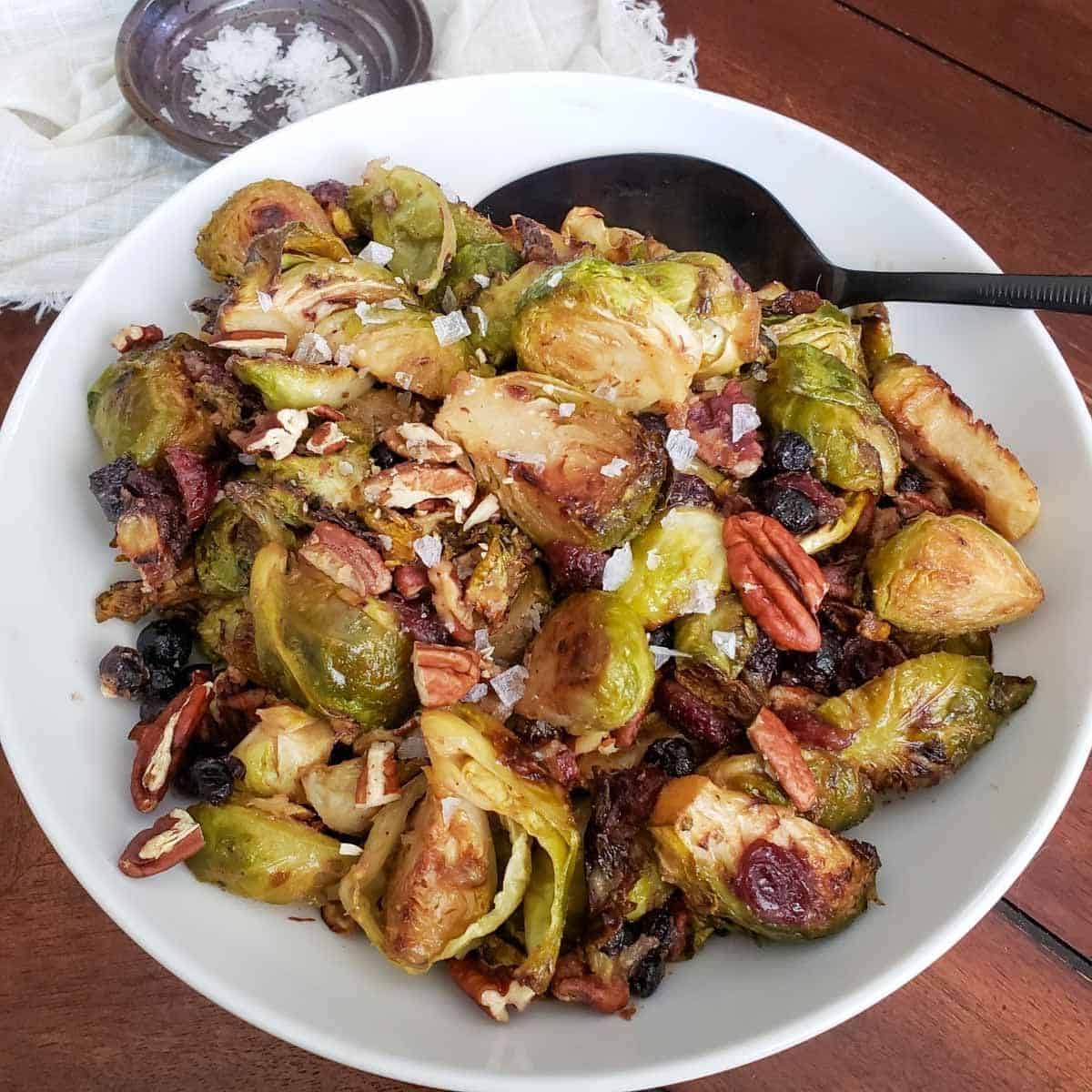 Roasted Brussel Sprouts With Cashew Butter n a white bowl with a serving spoon.