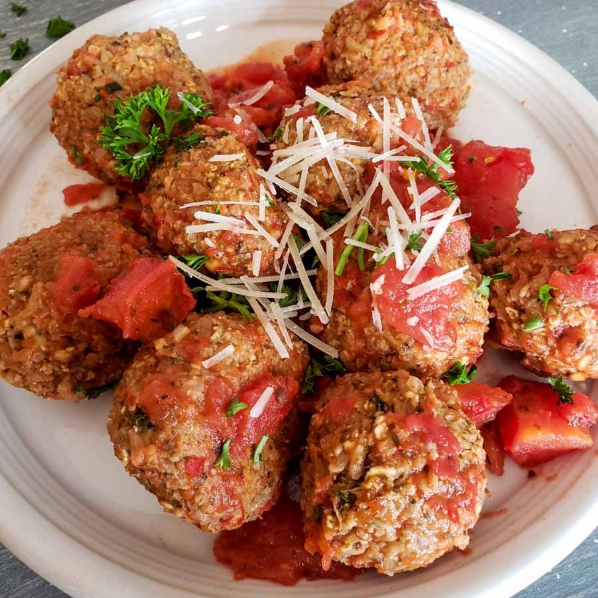 Vegetarian meatballs with cheese on top on a white plate. 