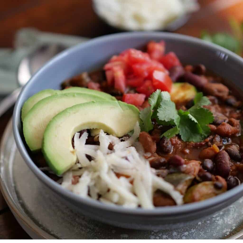 3 bean chili in a grey bowl with toppings. 