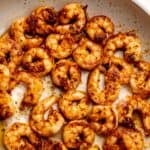Blackened shrimp with butter in a grey pan.