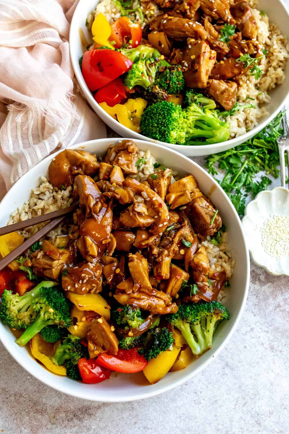 Teriyaki chicken thighs in a white bowl with chopsticks. 