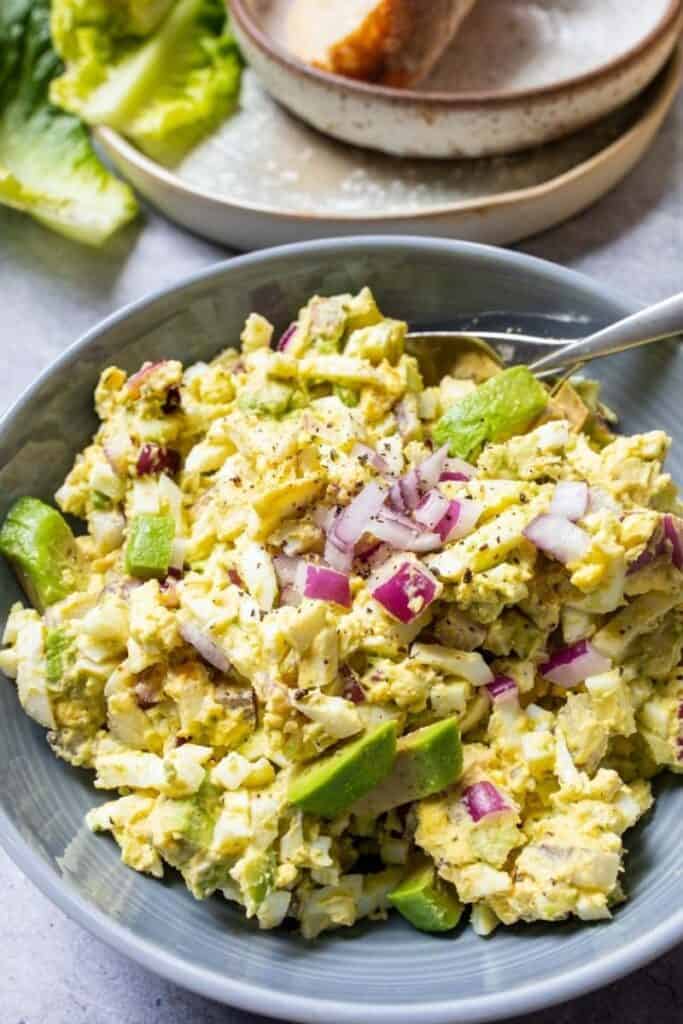 Egg salad in a gray bowl with bread and a spoon.