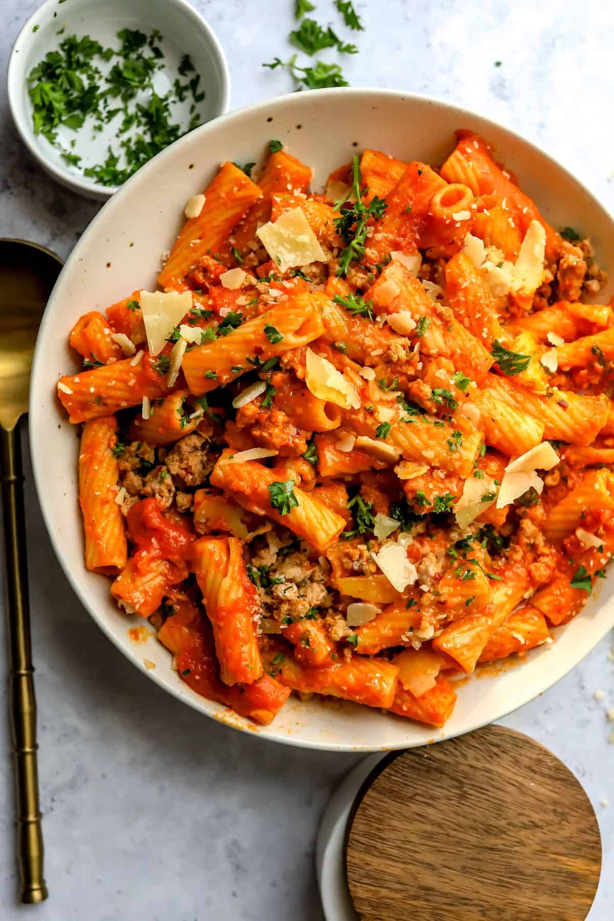 Big ceramic bowl with a spoon to the side filled with pumpkin pasta sauce.