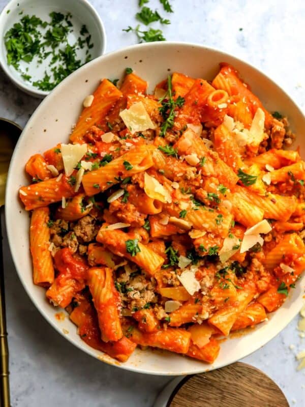Big ceramic bowl with a spoon to the side filled with pumpkin pasta sauce.