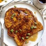 A slice of pumpkin french toast on a plate topped with pumpkin seeds.
