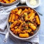 Grey pottery bowl with noodles and pumpkin sauce and a silver fork.