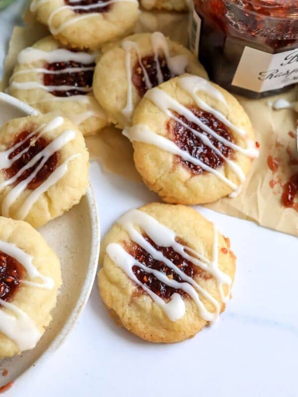 Raspberry Thumbprint Cookies on a white plate with jam on the side.