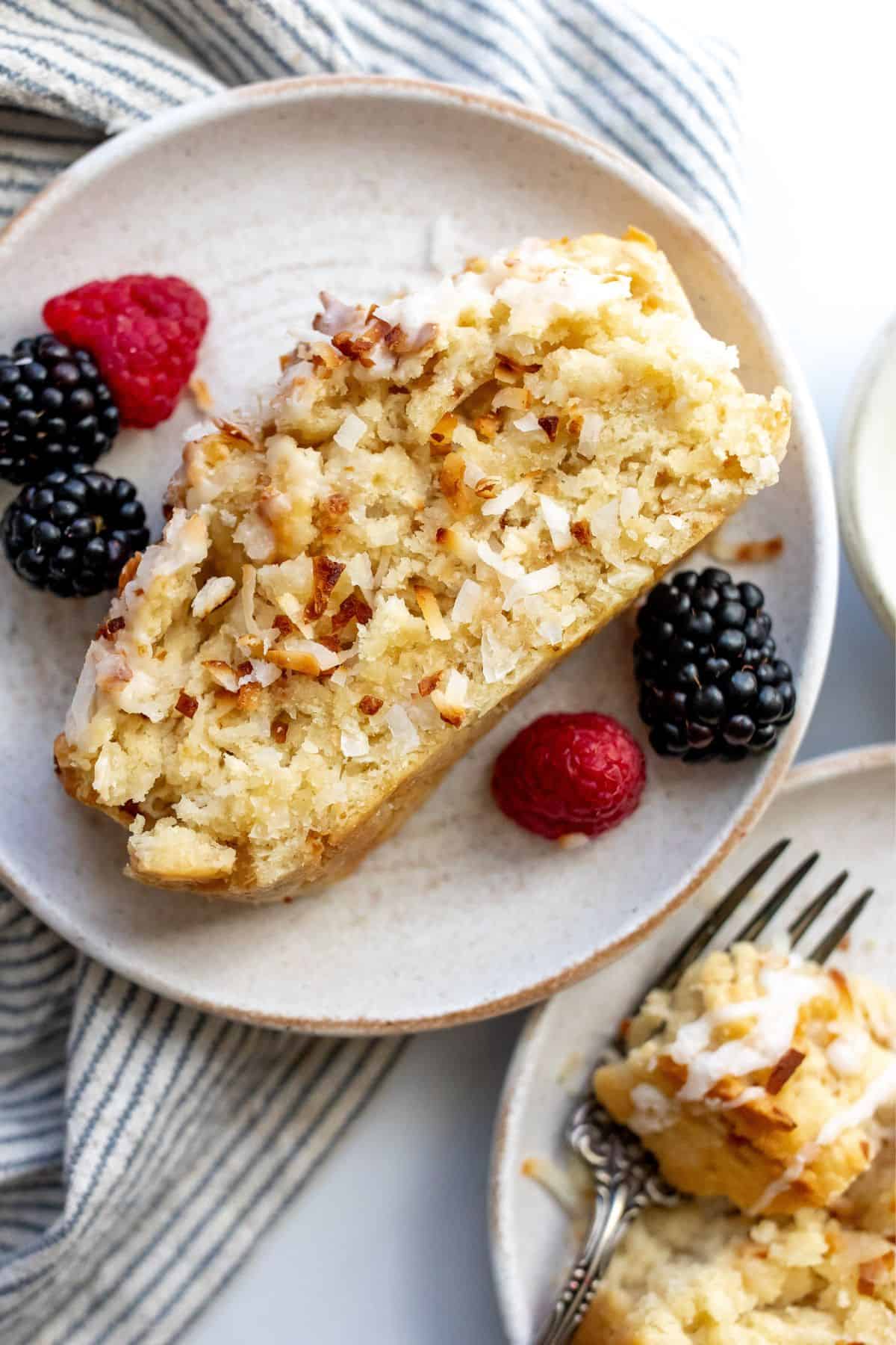 Coconut bread on a white plate with berries and a fork to the side. 