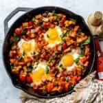 Black skillet with Sweet potato hash in it and eggs on top.