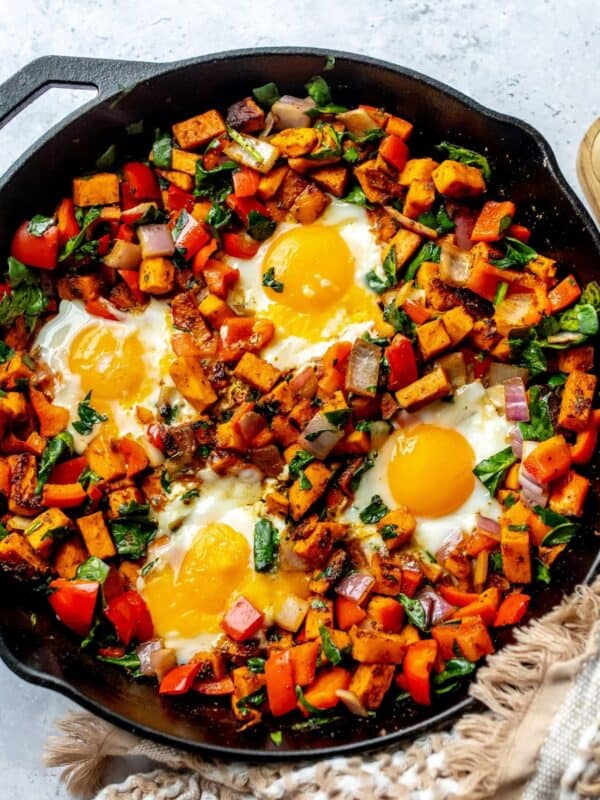 Black skillet with Sweet potato hash in it and eggs on top.