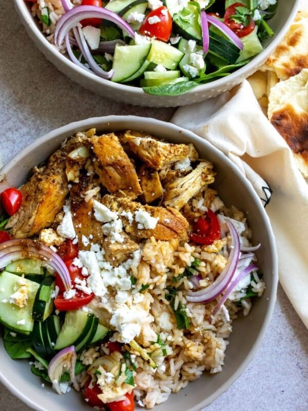 Mediterranean Bowl With Chicken and rice on a table with a bowl of greens in the top and pieces of pita to the side.