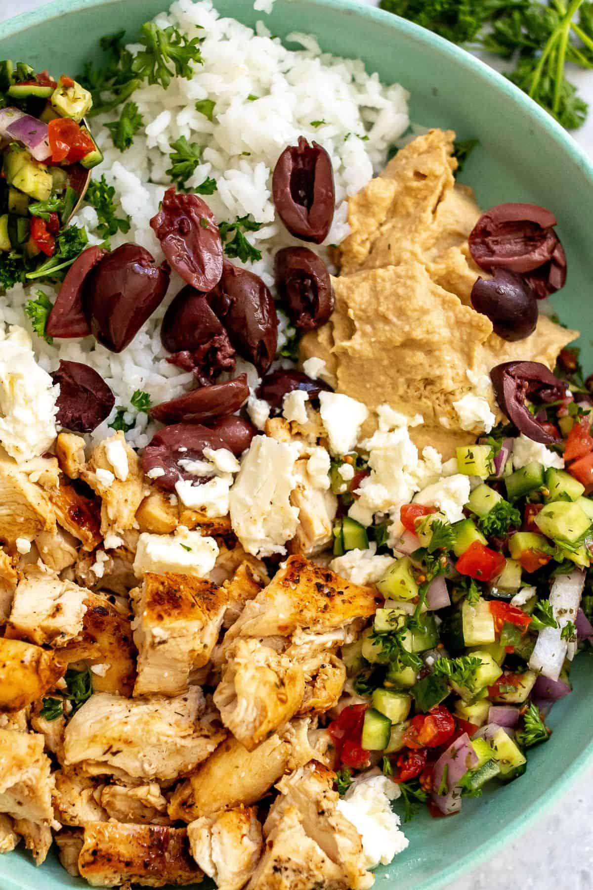 Mediterranean Bowl With Chicken and rice on a table with a bowl of greens.