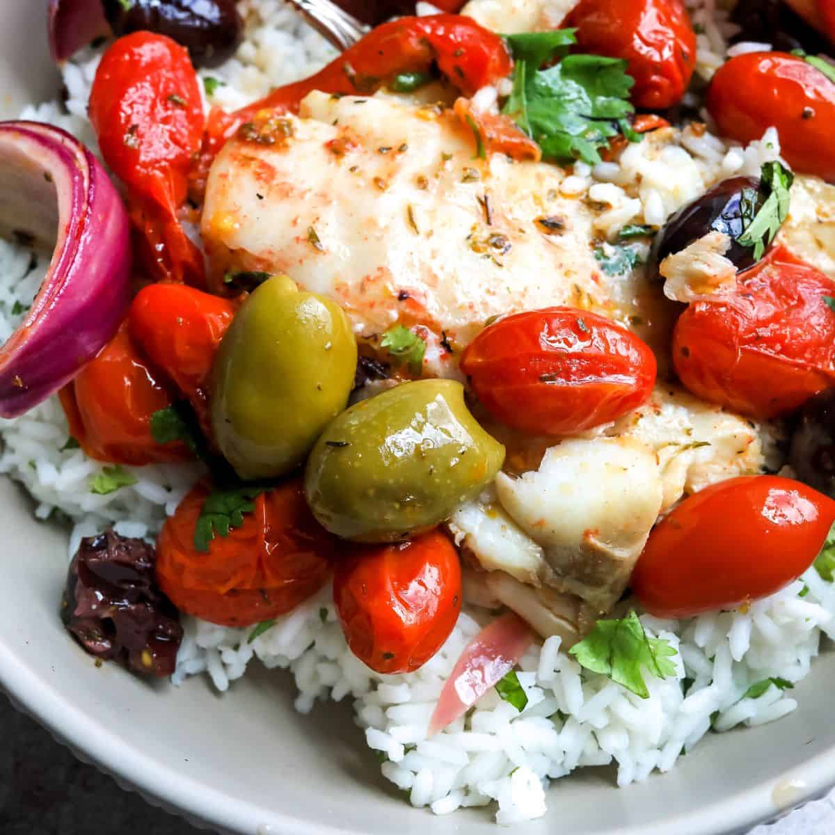 Baked white fish in a dish over rice with olives and tomatoes.