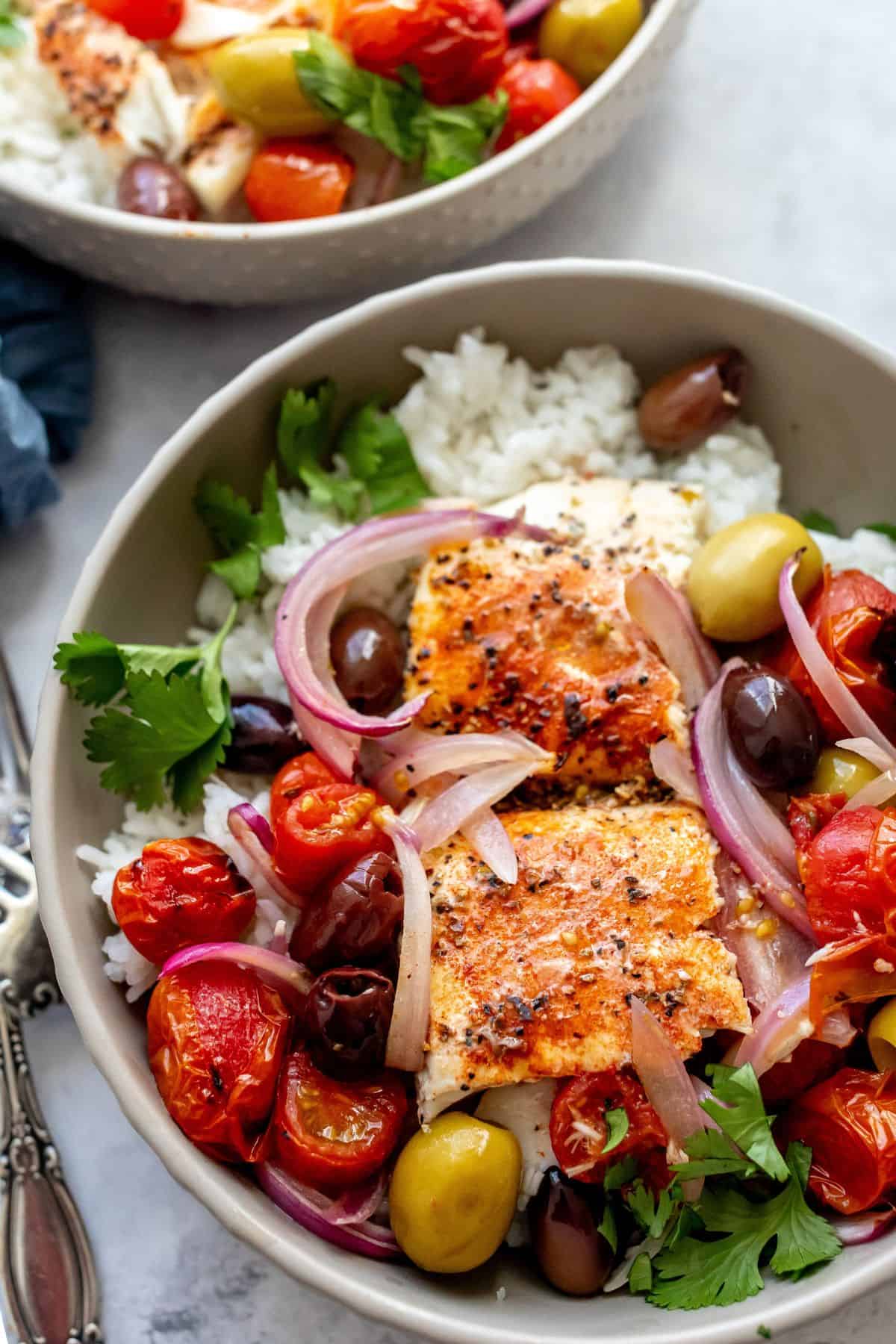 Bowls with Mediterranean Baked Fish in them and lots of olive served over rice with a silver fork.