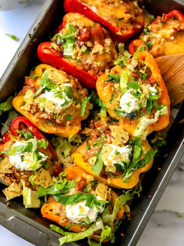 Baking dish with taco stuffed peppers in it and a wooden spatula.