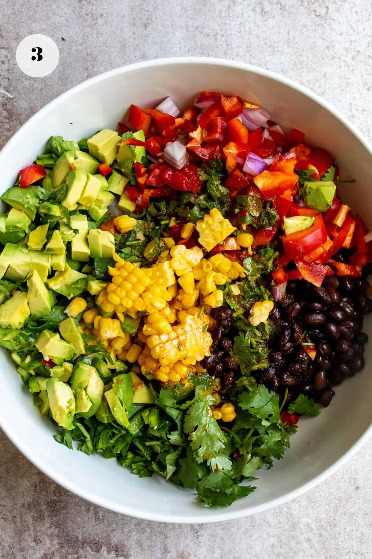 Avocado Mexican corn salad in a large serving bowl with a spoon.