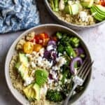 Veggies and quinoa in a grey bowl with a silver fork and toppings.