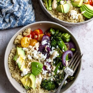 Veggies and quinoa in a grey bowl with a silver fork and toppings.