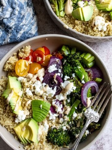 Veggies and quinoa in a grey bowl with a silver fork and toppings.
