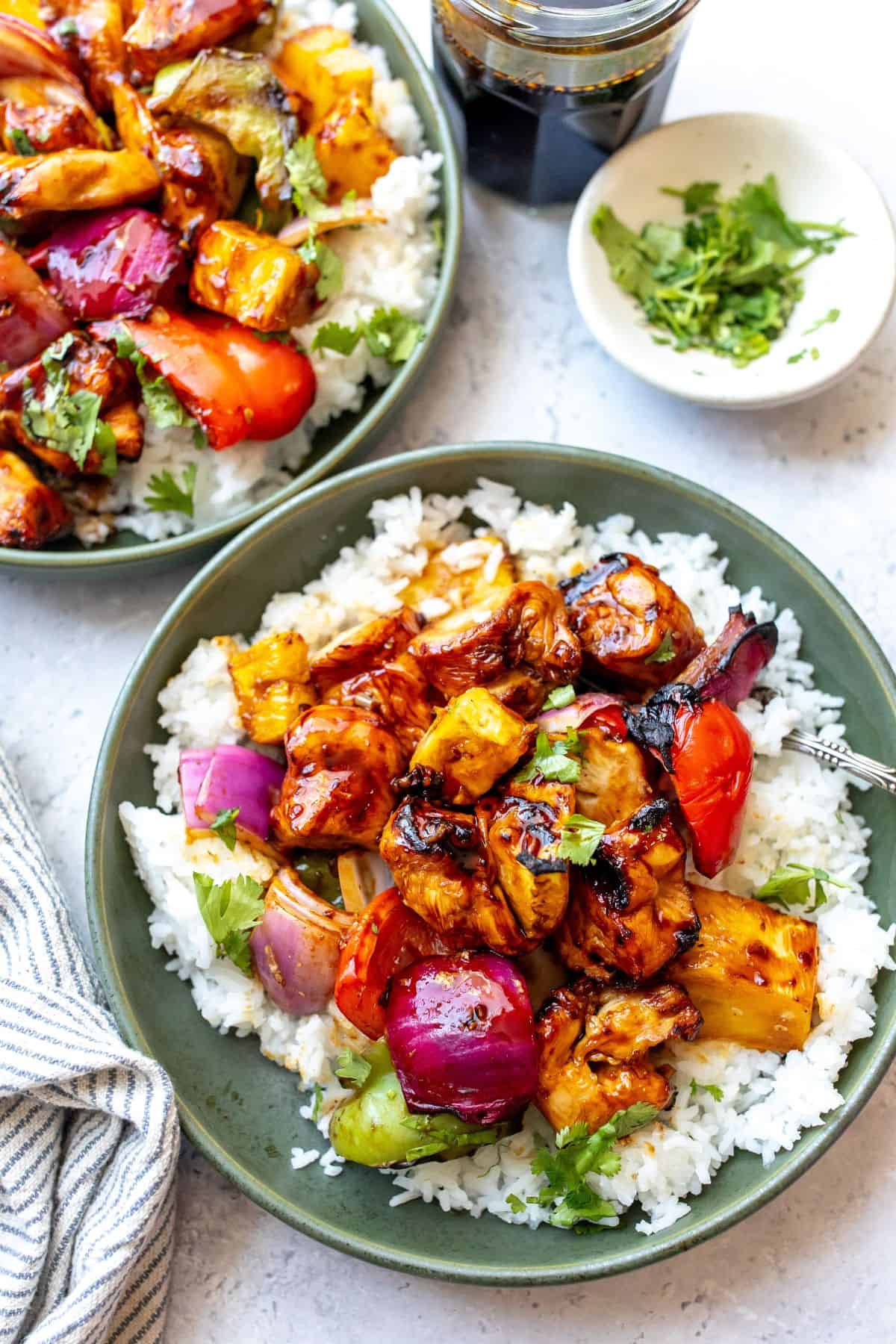 Green bowls with Teriyaki Chicken Skewers and rice. Sauce on the side.