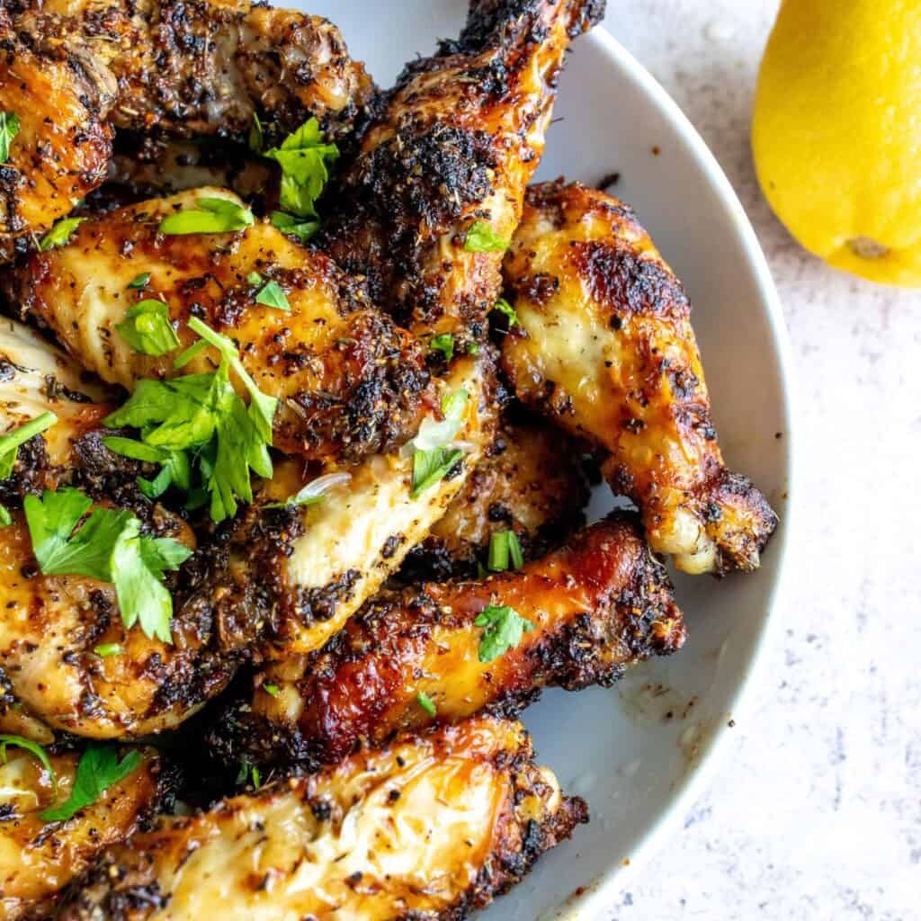 wings with lemon pepper in a white bowl with lemon and parsley. 
