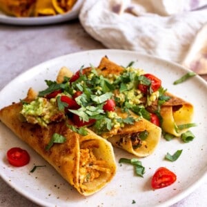 Baked Taquitos on a white plate with toppings.