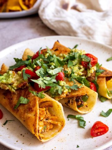 Baked Taquitos on a white plate with toppings.