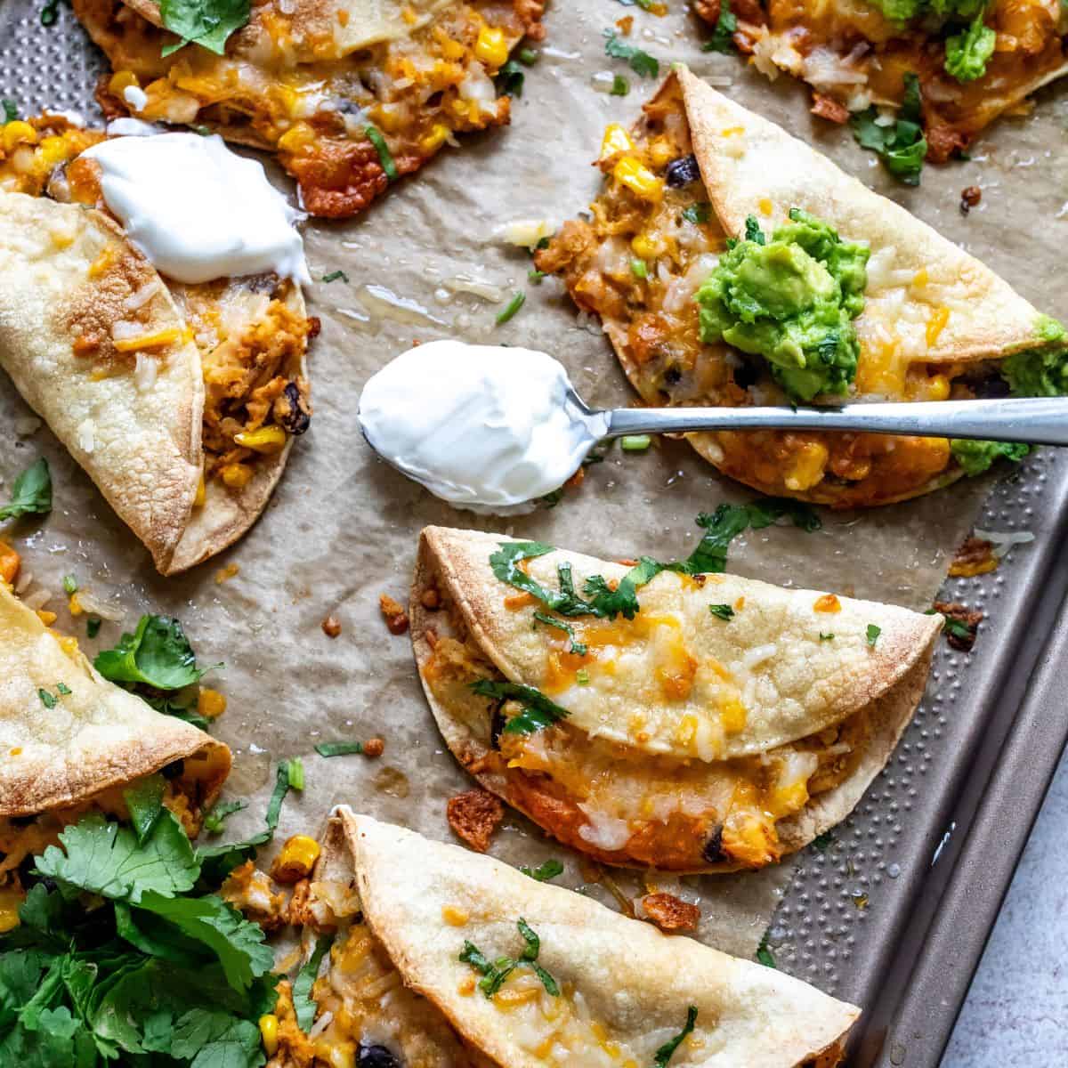 Crispy Chicken Tacos on a baking sheet with guacamole.